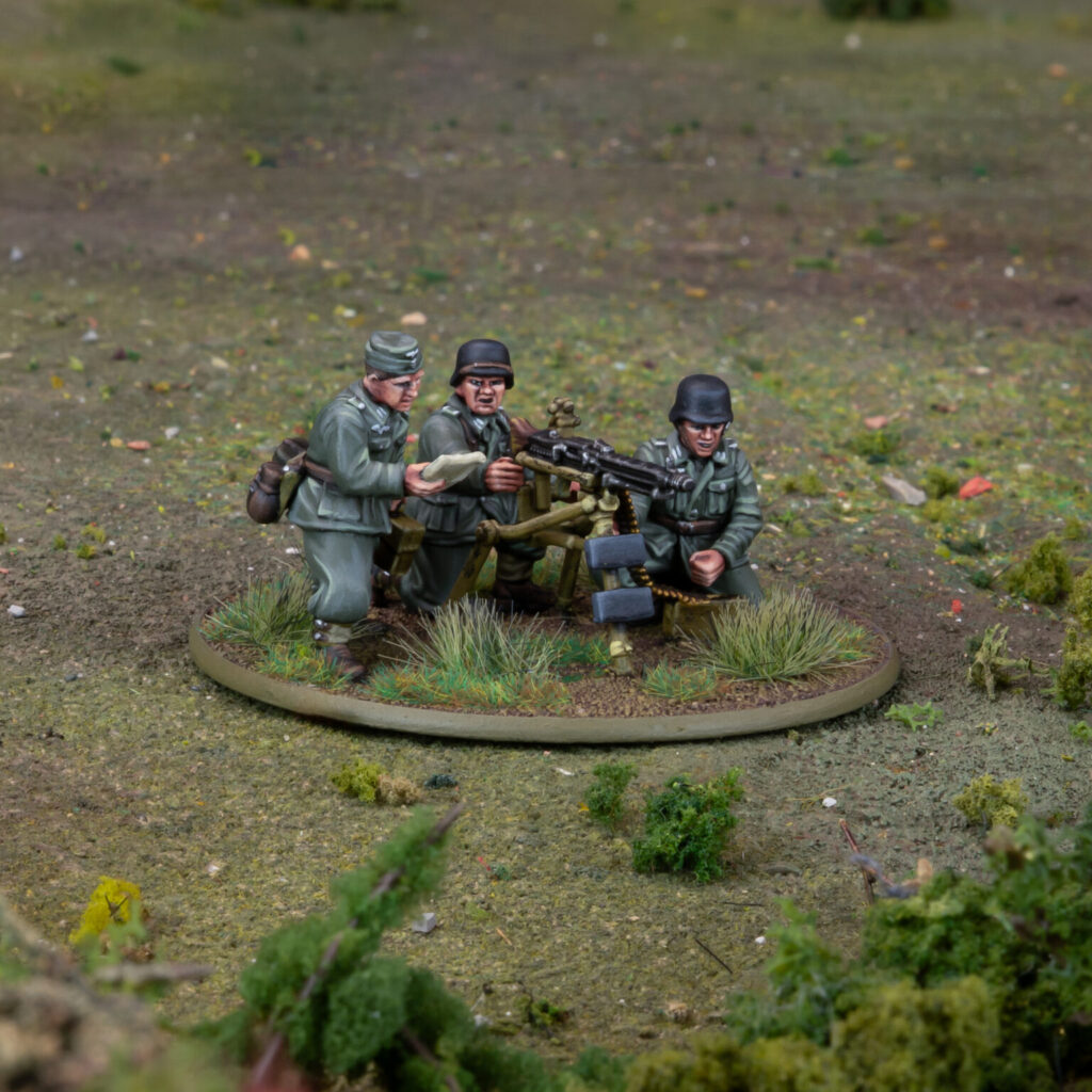 Miniature WWII soldiers operating a heavy machine gun on a grassy diorama base.