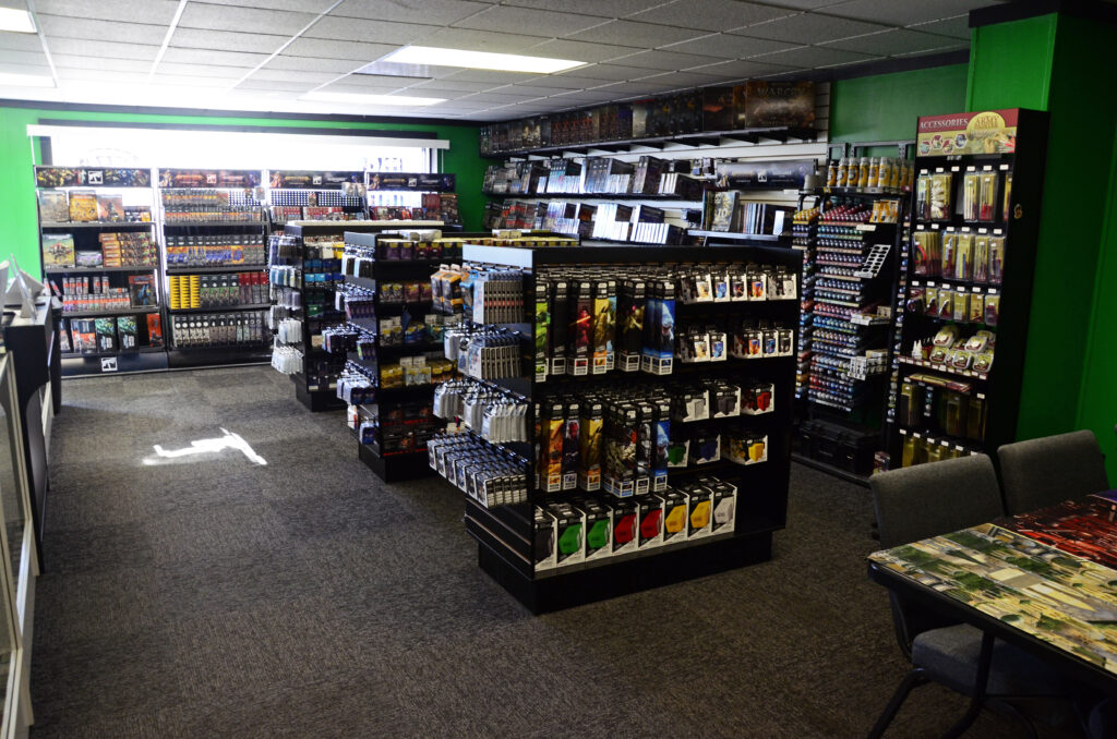 Bright game store interior with shelves of board games and video games, green walls, and a seating area on the right.