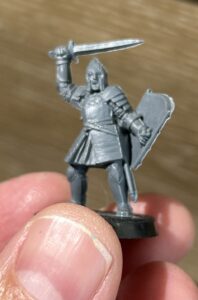 Medieval knight miniature in armor, raising a short sword with a shield at the side, mounted on a small base.