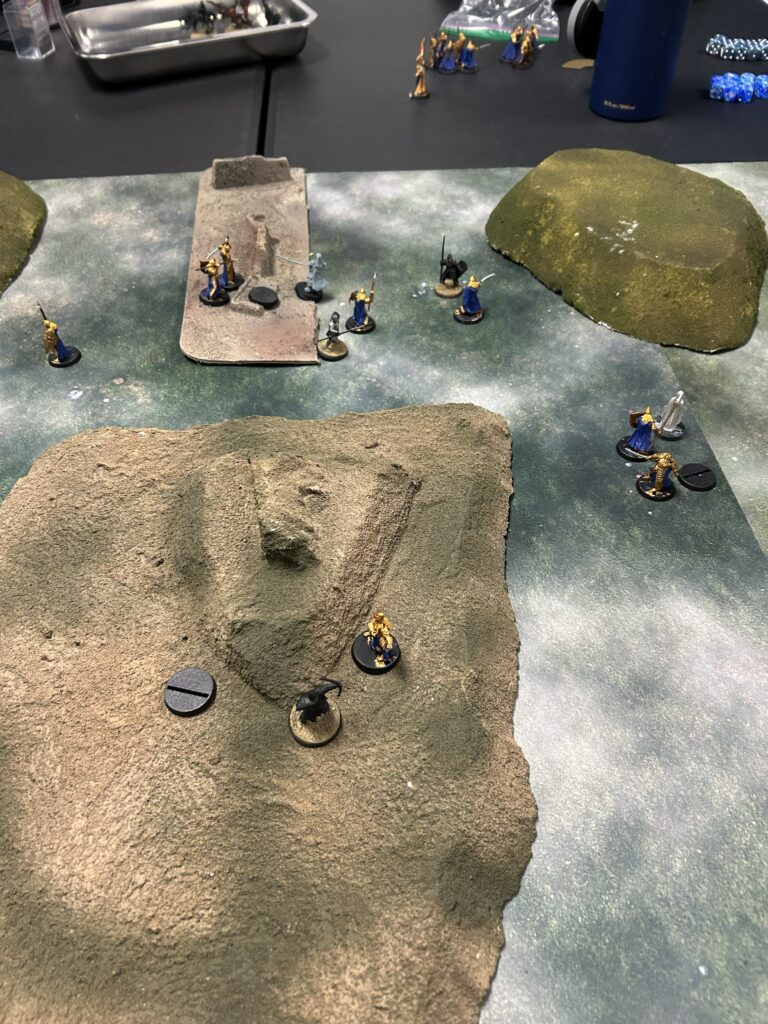 Tabletop wargame scene with painted miniatures on rocky terrain and a rugged battlefield mat.