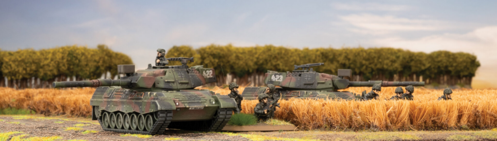 image Frontline Gaming Miniature diorama of two green tanks with soldiers in a wheat field, with trees in the distance.