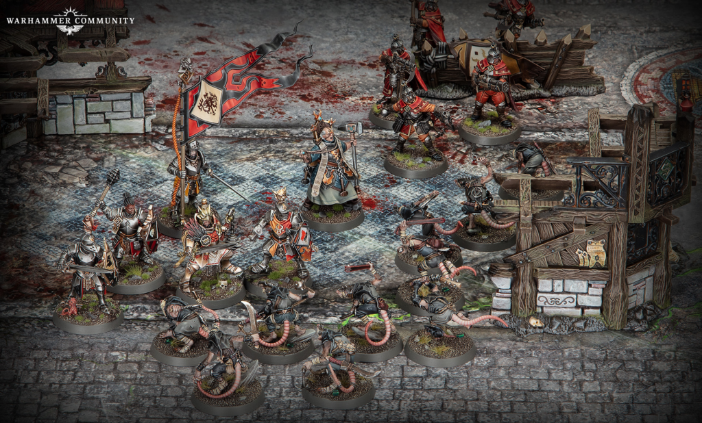 Group of Warhammer miniatures in armor on a ruined cobblestone battlefield, centered around a banner bearer with a hammer and shield.
