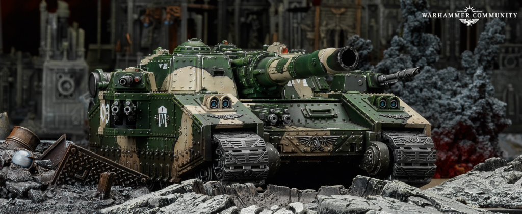 Green armored battle tank model with riveted plates and large cannon, set among rubble in a ruined battlefield scene (Warhammer Community)