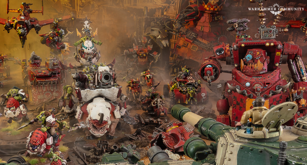 Massive Warhammer battle scene with green orks clashing against red armored machines in a dusty, industrial battlefield.