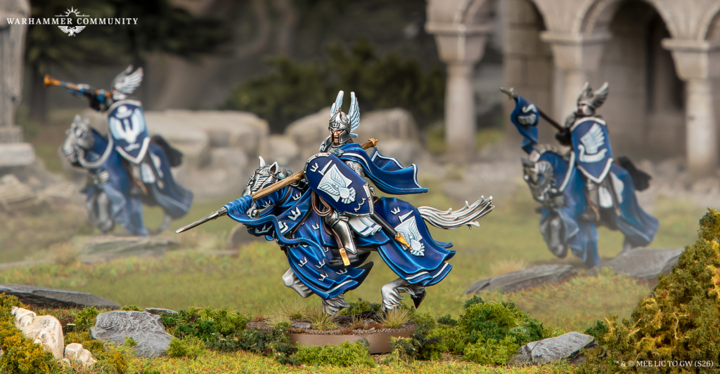 Blue and silver Warhammer cavalry miniature charging across a grassy diorama battlefield with ruins in the background and a Warhammer Community logo in the corner.