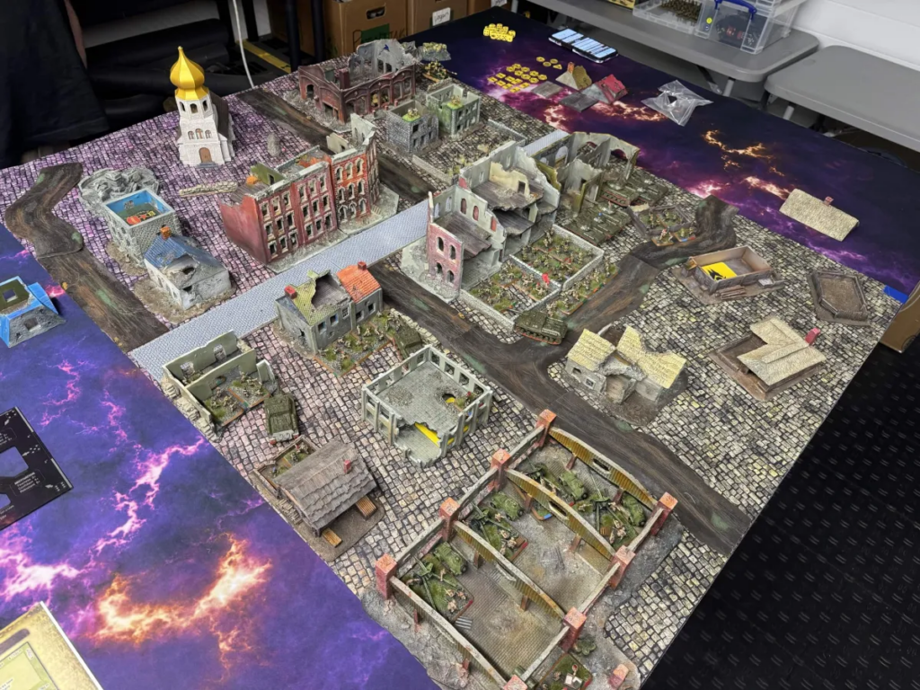 Tabletop wargame battlefield with ruined city blocks, narrow roads, and trenches on a printed mat.