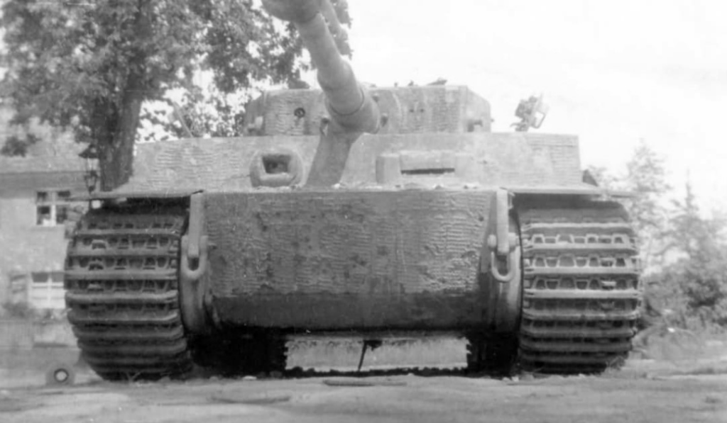 Front view of a muddy tank with a long gun barrel, low to the ground, tracks visible on each side.