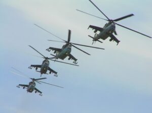 Four helicopters in tight formation flying through a blue sky.