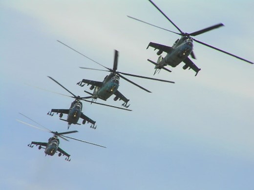 Four helicopters in tight formation flying through a blue sky.