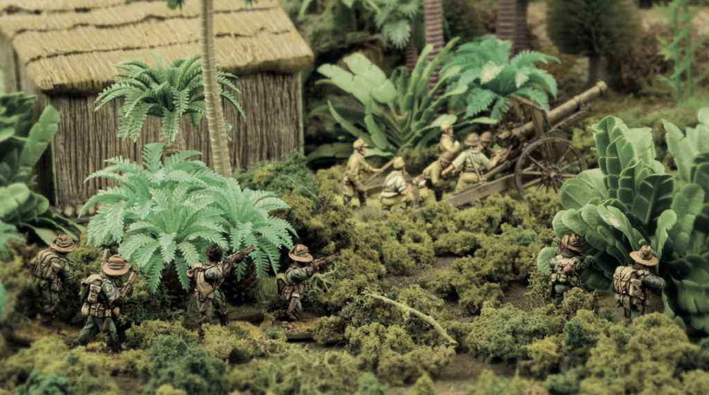 Miniature war diorama: soldiers advancing through jungle toward a cannon near a thatched hut.