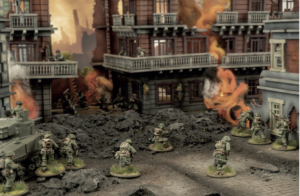 Miniature World War II battle scene with soldiers advancing through a ruined city, smoke and flames erupting from destroyed buildings.