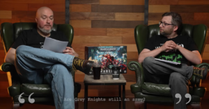 Two men in green leather chairs discuss on a studio set; a Warhammer 40K box sits on the table between them, caption: 'Are Grey Knights still an army?'