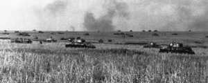Line of tanks moving across a grassy field with smoke rising on the horizon.