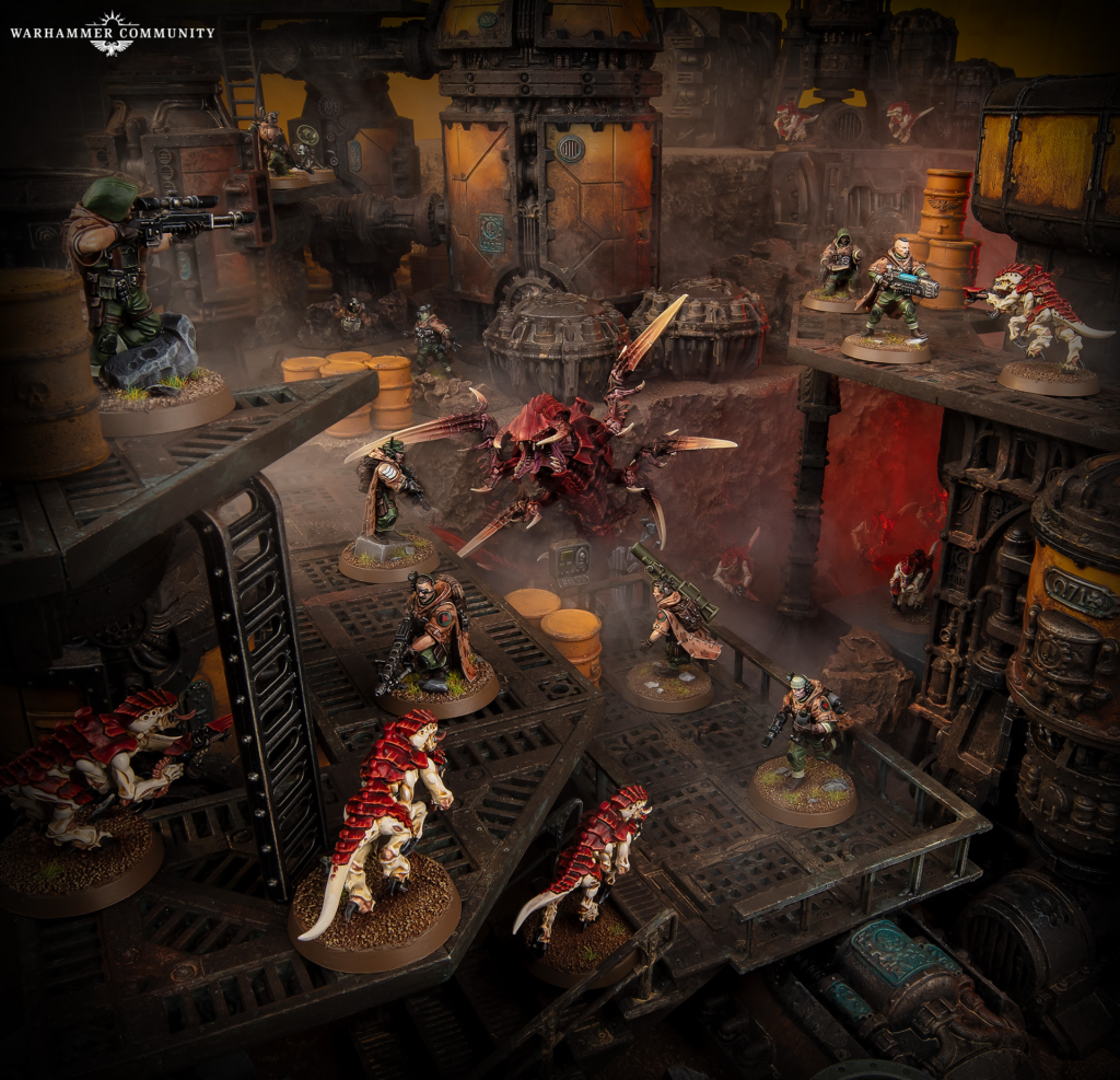 Tabletop Warhammer battle scene with armored troops fighting red, dinosaur-like aliens amid large rusted machinery and crates.