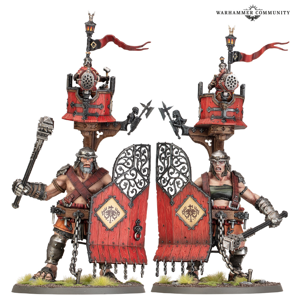 Two Warhammer fantasy miniatures: back-to-back barbarian warriors behind red wooden shields, with armored weapons and small siege-tower structures overhead.