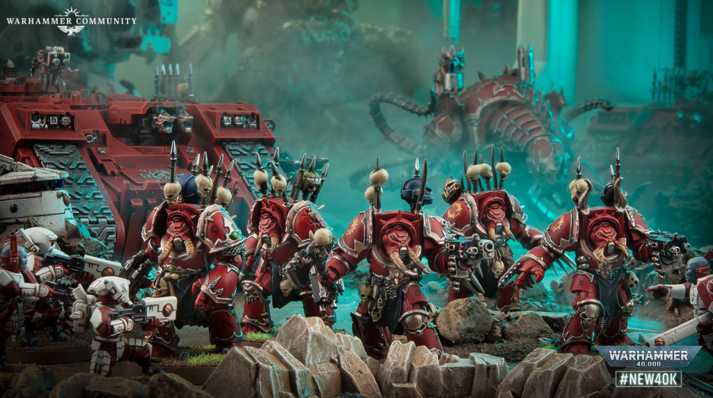 Warhammer 40,000 diorama with rows of red-armored Space Marines advancing across rocky ground, tanks in the background.