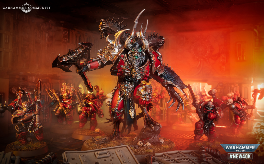 A towering Chaos demon in red and black armor with horns and spikes, flanked by smaller demons in a war-torn workshop.