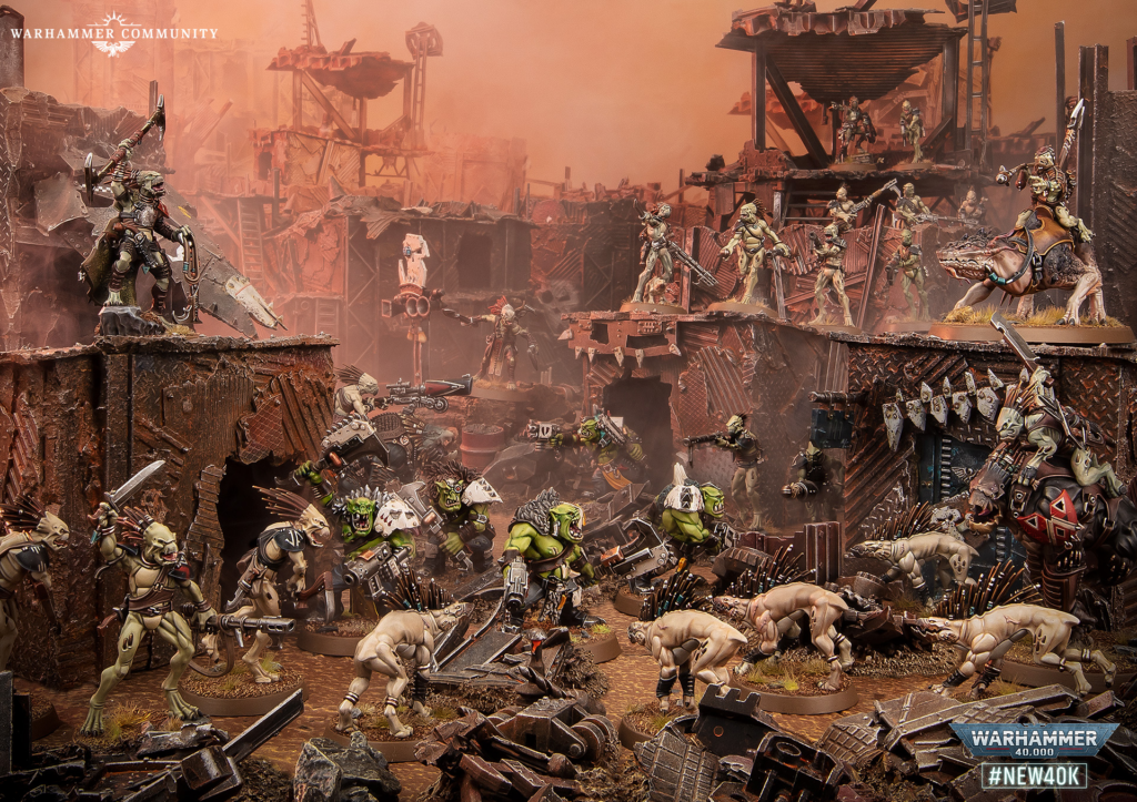 Warhammer battle diorama with orks vs humans amid rusted, crumbling ruins and orange smoke; figures on elevated platforms and a mounted rider on a beast far right