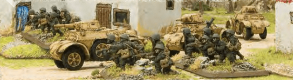 Military diorama showing soldiers advancing with armored vehicles near small white buildings in a rural setting.
