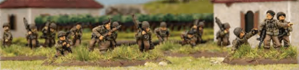 Miniature toy soldiers advancing across a grassy battlefield near small village buildings in the background.