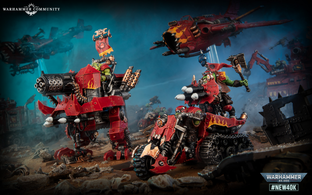 image Frontline Gaming Orc Warhammer 40k battle scene with red armored machines firing multi-barrel guns amid rocky debris and blue smoke in the background.