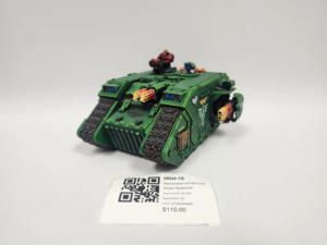 Green armored model tank with a small red figure on top, displayed on a white surface with a price tag showing $110 and a QR code nearby.