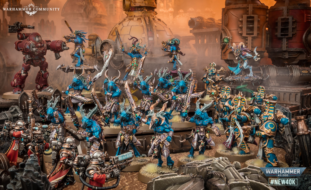 image Frontline Gaming Dramatic Warhammer 40,000 battle scene with numerous blue-armored warriors clashing around a large red siege mech amid dusty, industrial machinery.
