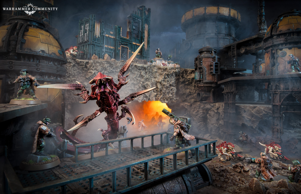 Warhammer diorama of armored soldiers battling a large red multi-armed monster on a rocky, smokey industrial battlefield.