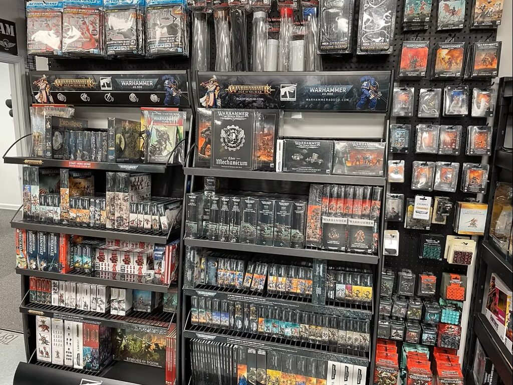 Retail display of Warhammer 40,000 tabletop game products on black shelves, with boxed sets, rulebooks, and miniatures arranged in multiple rows.