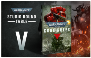 Promotional banner for Warhammer 40,000 Studio Round Table, with a large white 'V' on the left and a Core Rules hardcover featuring a red-armored figure against a fiery battle scene on the right.