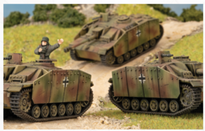 Diorama scene with three WWII-model tanks on a dirt road; a standing soldier figure waves from the left tank as a camouflaged vehicle rolls uphill in the background.