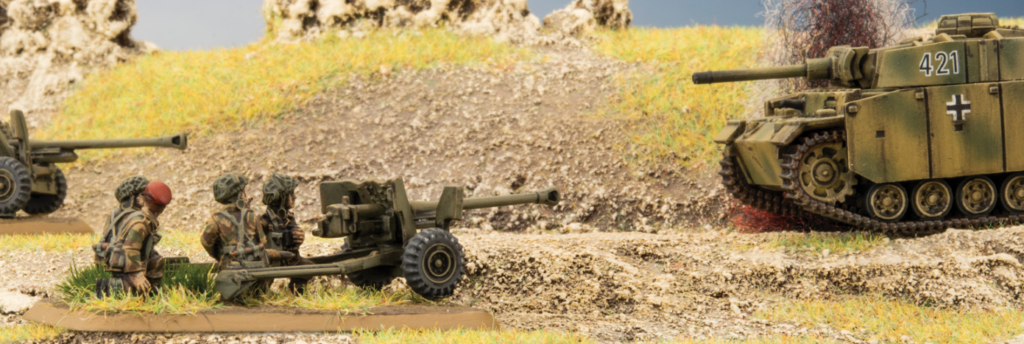 Soldiers load a towed field gun as a camouflaged tank rolls along a dirt road in the background.