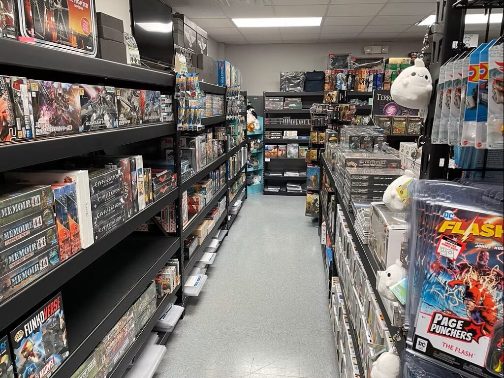 A store aisle filled with shelves of board games, puzzles, and collectibles on both sides, lit by fluorescent ceiling lights.