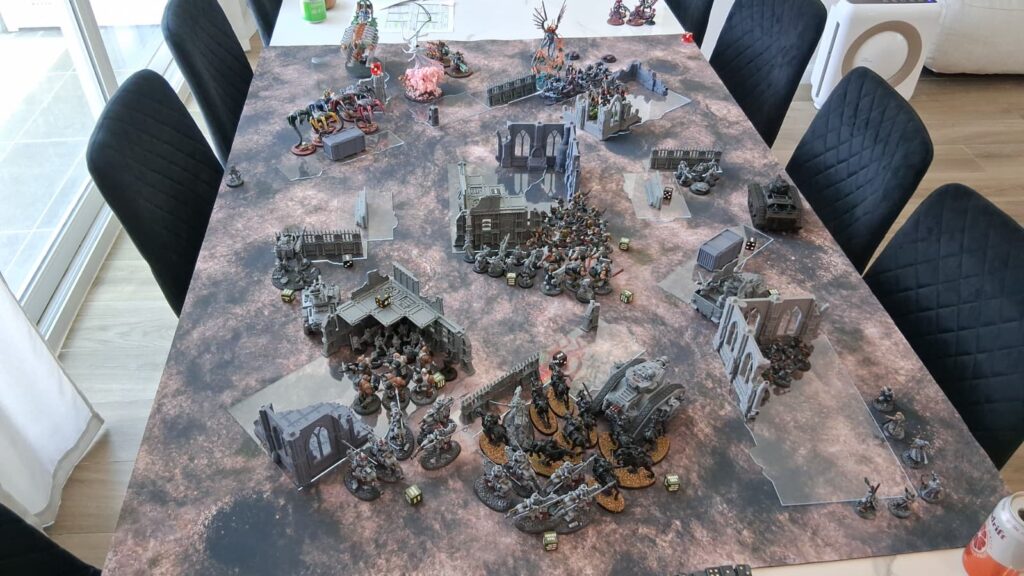 WhatsApp Image 20260614 at 10130 PM Frontline Gaming Tabletop wargaming battle scene with modular terrain and numerous miniature figures arranged on a large game table.