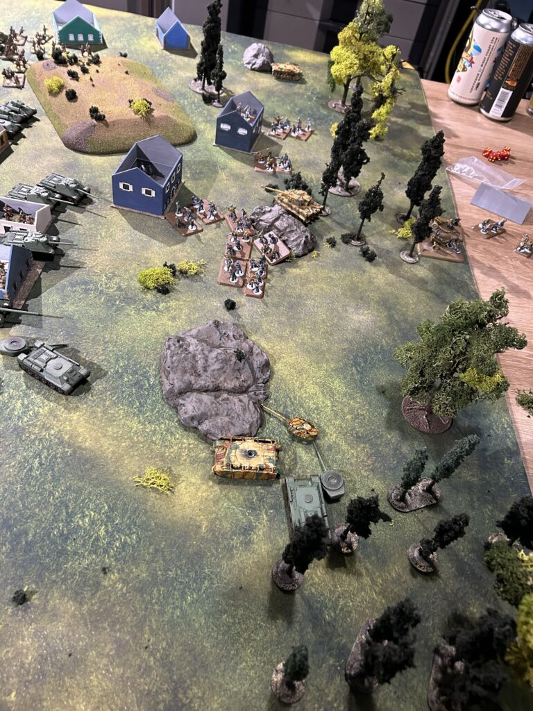 Tabletop wargame battlefield with blue houses, tanks, infantry, and trees on a grassy map ️🏟️