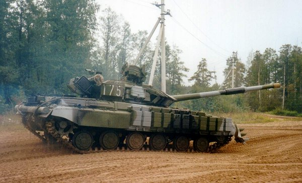 image Frontline Gaming Green military tank on a dusty dirt road, smoke rising, turret pointed to the right with a wooded backdrop behind.