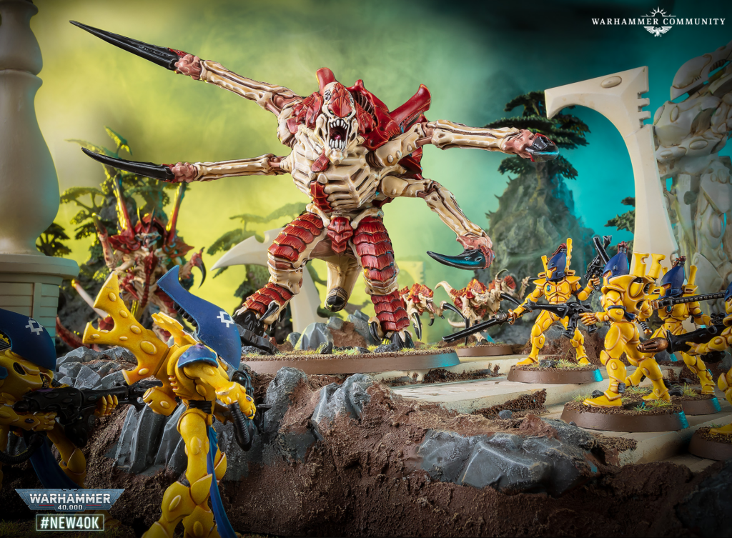 Centerpiece red multi-armed demon lunges over a rocky diorama, surrounded by yellow armored figures in battle; Warhammer branding visible in the scene.