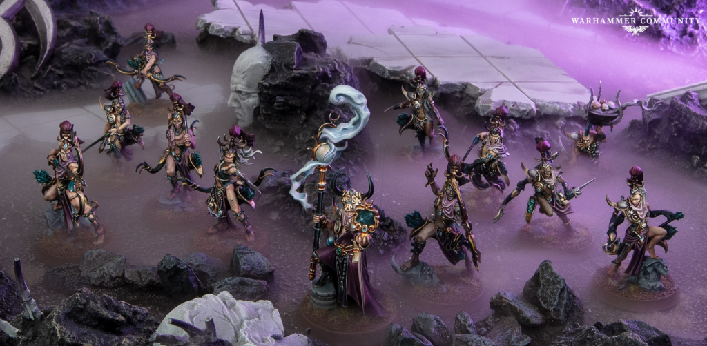 Group of ornate fantasy miniatures on a rocky battlefield with purple fog; Warhammer Community logo top-right.