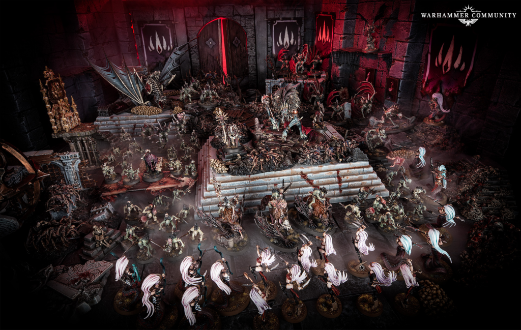 Wide view of a Warhammer battle diorama with demons, armored troops, and winged monstrosities raging on ruined, stair-stepped platforms in a crimson dungeon setting.