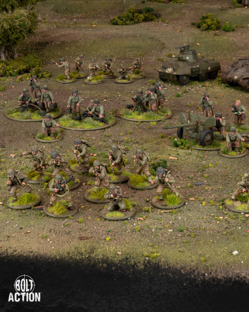 image Frontline Gaming Group of miniature WWII soldiers advancing across a dirt battlefield with small green tanks and tufts of grass, Bolt Action logo bottom left.