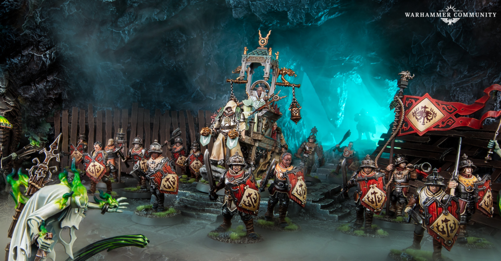 Warhammer fantasy battle diorama with armored troops marching in a cavern, led by an ornate throne-like carriage and banners.