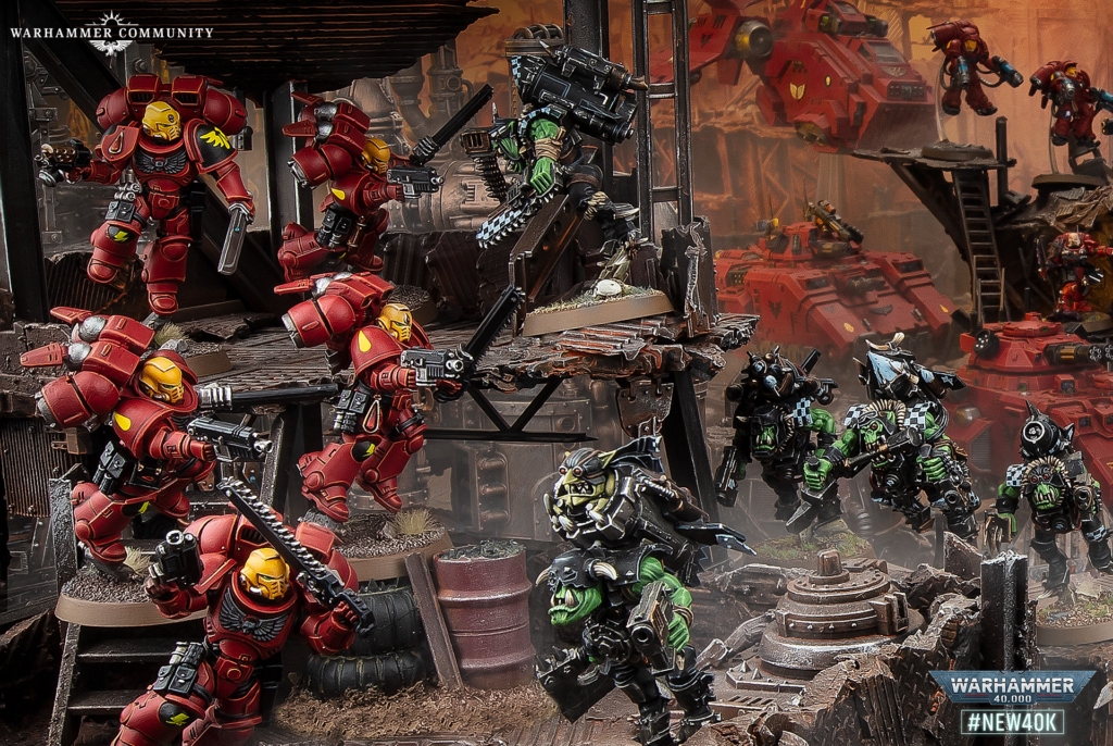 Warhammer 40,000 battle diorama with red Space Marines fighting green Orks amid ruined industrial structures, logo in corner.