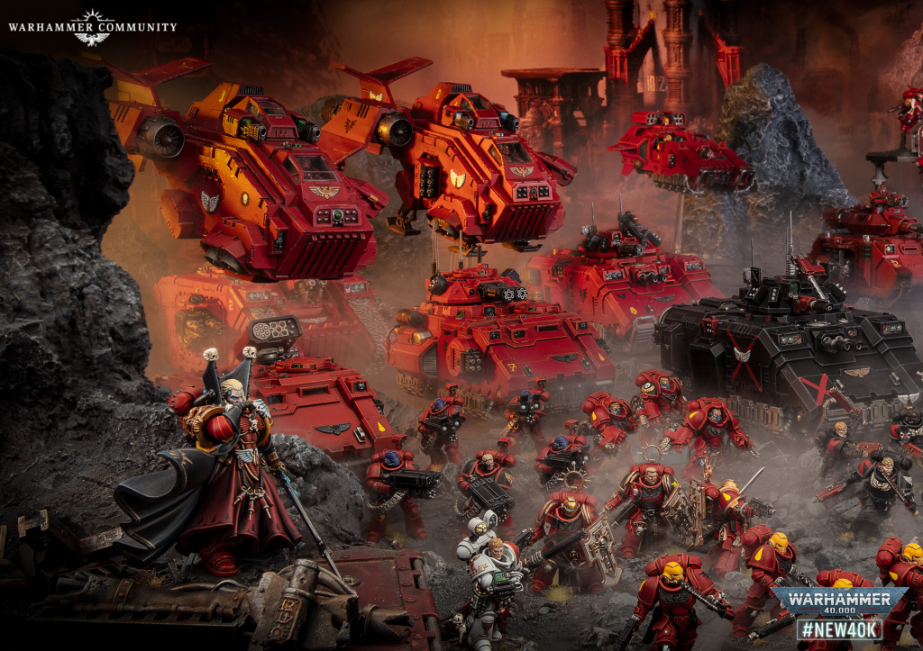 Red Warhammer 40,000 battle scene with large red tanks and infantry advancing through a rocky, smoky battlefield with ruins in the background and Warhammer Community branding in the corner.