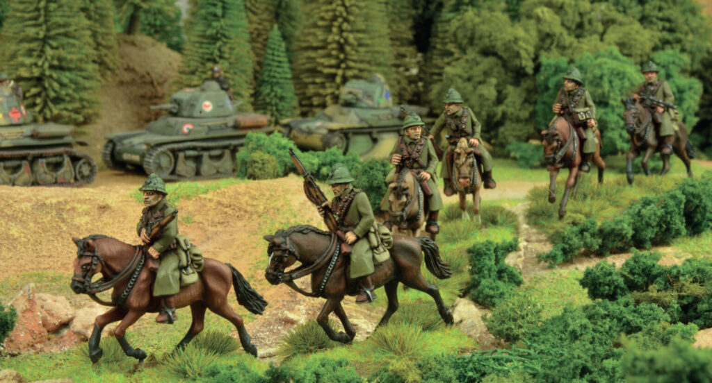 Model military diorama soldiers on horseback advancing through a forested landscape with tanks in the background