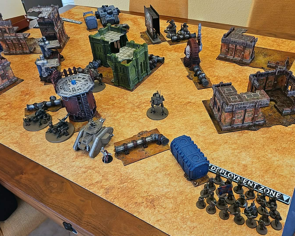 Tabletop wargame setup on a textured table with ruined buildings miniatures and a blue transport pod players figures and terrain spread across a battlefield