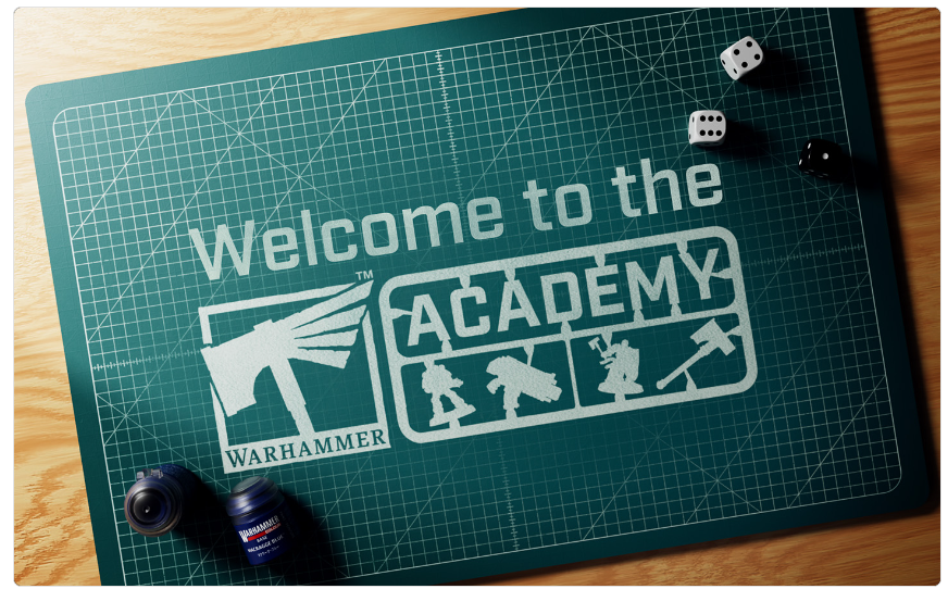 Green cutting mat showing Welcome to the Academy with the Warhammer logo and small hobby silhouettes in a game studio setup