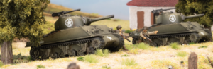Two WWII era tanks in a rural diorama with soldiers crouching beside them on dry grassland