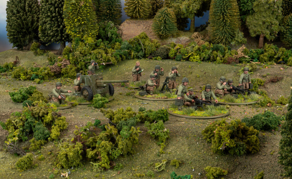 Miniature World War II scene with soldiers operating a field gun in a wooded area in a diorama setting