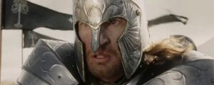 Man wearing a metallic medieval helmet and armor, grimacing, in a battle-ready pose.