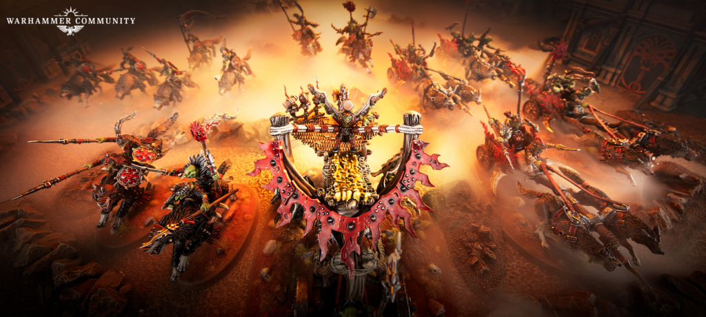 Warhammer Community logo in the top-left; a fiery battle scene with a central spiked siege vehicle and red-plated armor-clad riders clashing in smoke and lava.